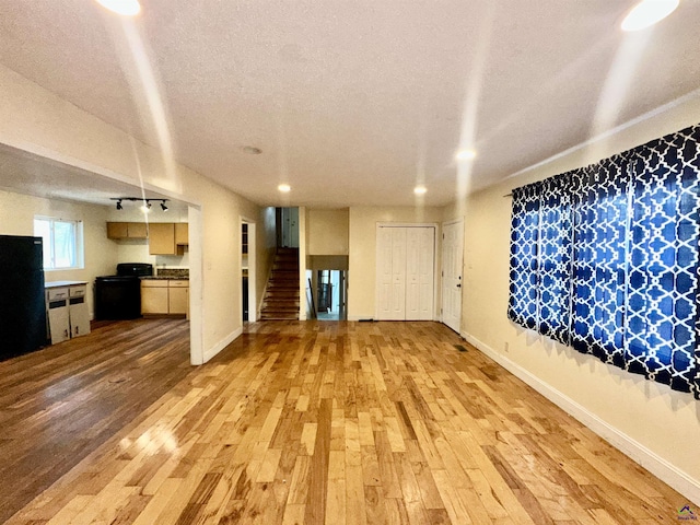 unfurnished living room with baseboards, a textured ceiling, light wood finished floors, and stairs