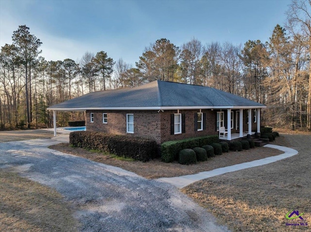 view of home's exterior with a porch, an attached carport, gravel driveway, and brick siding