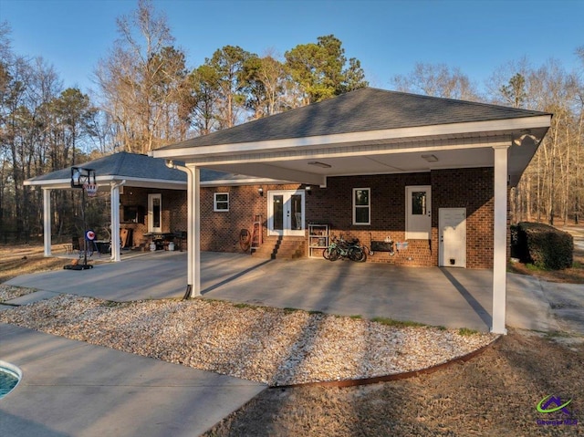 back of house featuring entry steps, an attached carport, brick siding, french doors, and roof with shingles