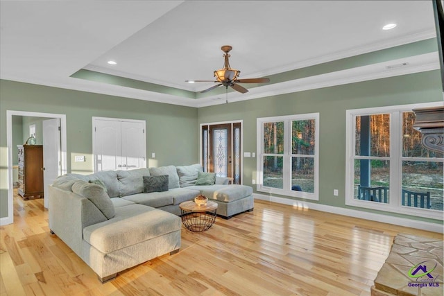 living area featuring light wood-style floors, ceiling fan, ornamental molding, and a raised ceiling