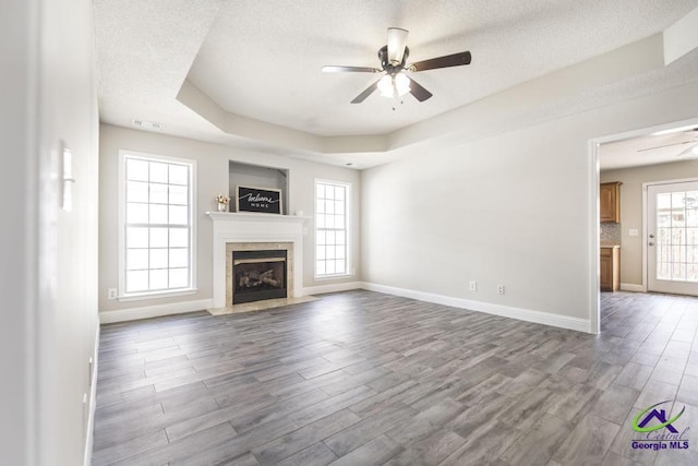 unfurnished living room featuring ceiling fan, a fireplace with flush hearth, wood finished floors, a tray ceiling, and a textured ceiling