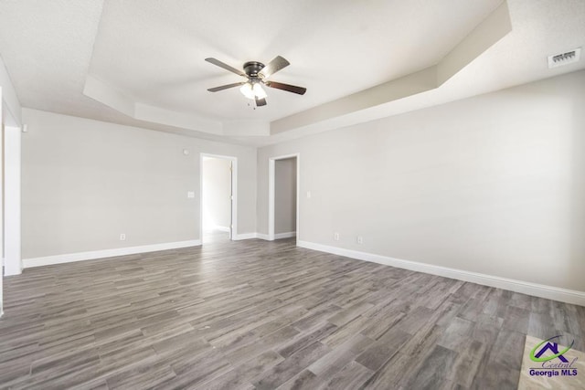 spare room with a tray ceiling, visible vents, baseboards, and wood finished floors