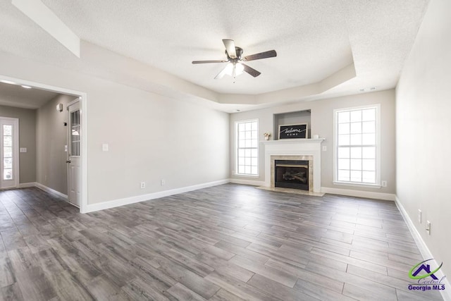 unfurnished living room featuring a textured ceiling, wood finished floors, a tile fireplace, and a raised ceiling