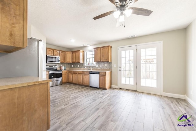 kitchen with visible vents, decorative backsplash, stainless steel appliances, light countertops, and light wood-style floors