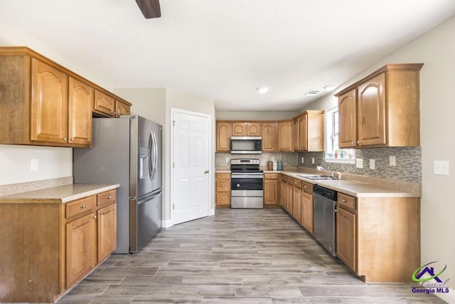 kitchen with stainless steel appliances, brown cabinets, a sink, and decorative backsplash