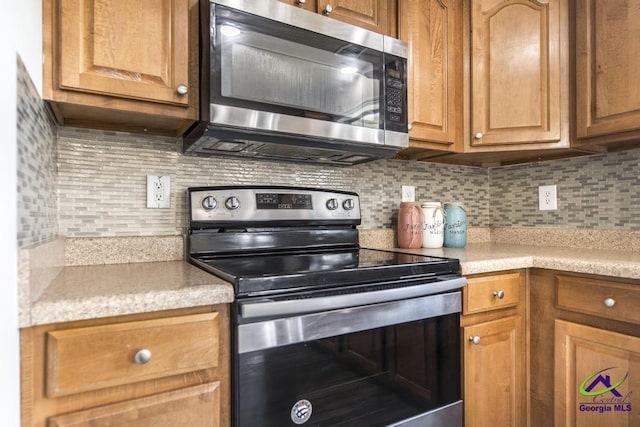 kitchen with brown cabinetry, appliances with stainless steel finishes, light countertops, and backsplash