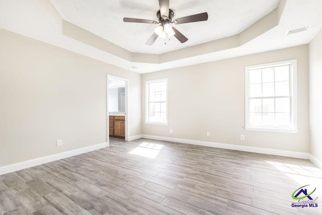 unfurnished bedroom with visible vents, baseboards, ensuite bathroom, a tray ceiling, and light wood-type flooring