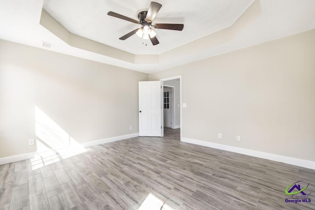 unfurnished room featuring ceiling fan, baseboards, a raised ceiling, and wood finished floors