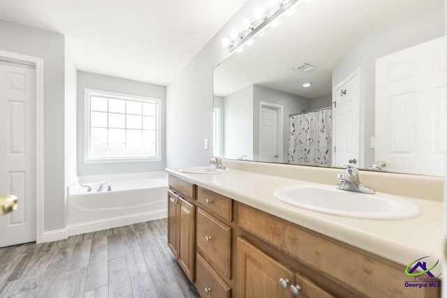 bathroom with a garden tub, visible vents, a sink, and wood finished floors