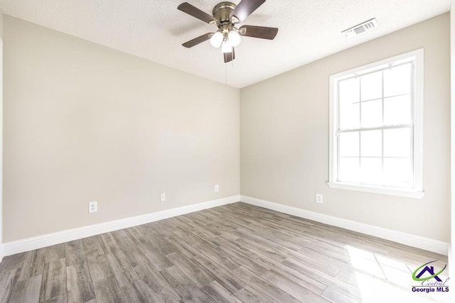 unfurnished room with plenty of natural light, wood finished floors, visible vents, and baseboards