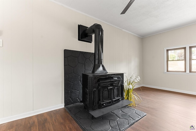 room details featuring baseboards, wood finished floors, a wood stove, and crown molding