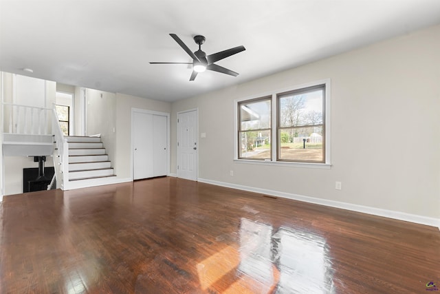 unfurnished living room featuring plenty of natural light, stairway, baseboards, and wood finished floors