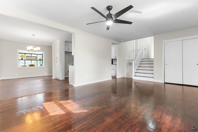 unfurnished living room with ceiling fan with notable chandelier, stairway, wood finished floors, and baseboards