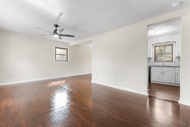 empty room with a sink, baseboards, dark wood-style flooring, and a wealth of natural light