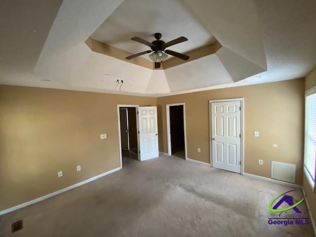 unfurnished bedroom with a ceiling fan, a raised ceiling, two closets, and baseboards