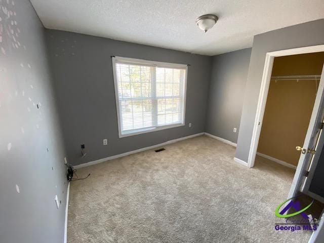 unfurnished bedroom with carpet floors, a closet, visible vents, a textured ceiling, and baseboards