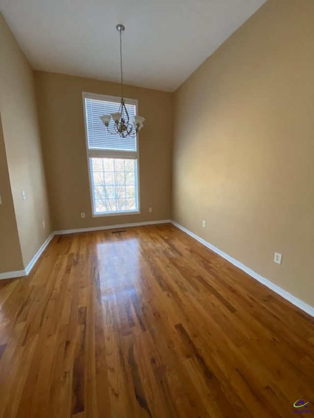 spare room with baseboards, a notable chandelier, and wood finished floors