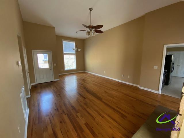 unfurnished living room featuring ceiling fan with notable chandelier, baseboards, and wood finished floors