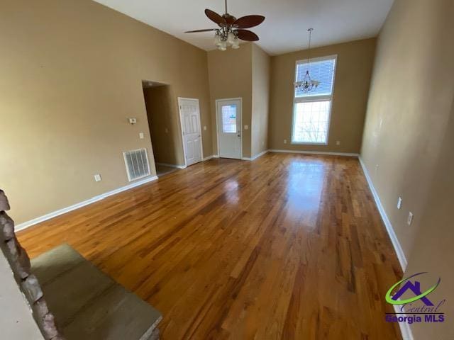 unfurnished living room featuring visible vents, a high ceiling, wood finished floors, baseboards, and ceiling fan with notable chandelier