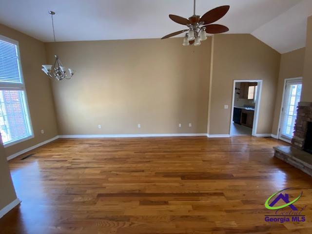 unfurnished living room with ceiling fan with notable chandelier, baseboards, wood finished floors, and a stone fireplace