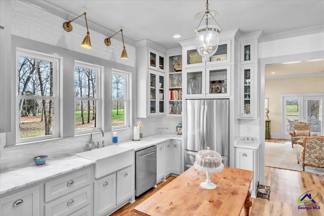 kitchen with white cabinetry, stainless steel appliances, a sink, and decorative light fixtures