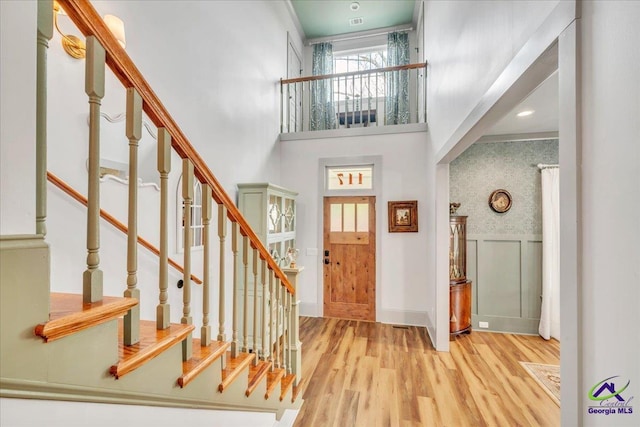 foyer entrance with a high ceiling, stairway, wainscoting, and wood finished floors