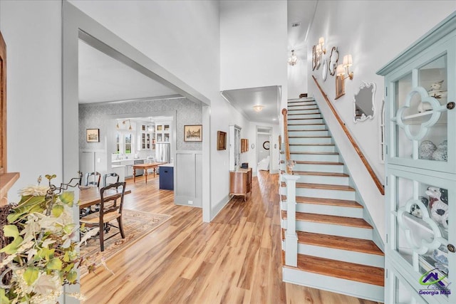 foyer entrance with a wainscoted wall, wallpapered walls, ornamental molding, light wood-type flooring, and stairs