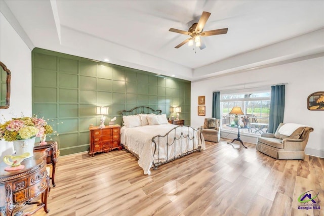 bedroom with a raised ceiling, light wood-style flooring, an accent wall, ceiling fan, and baseboards