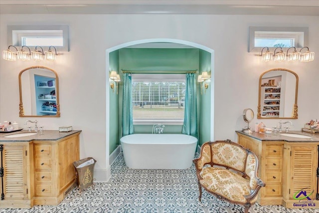 bathroom featuring two vanities, a soaking tub, and a sink