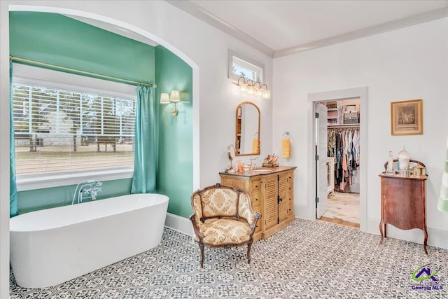 bathroom with a freestanding tub, a shower with shower curtain, vanity, baseboards, and a spacious closet