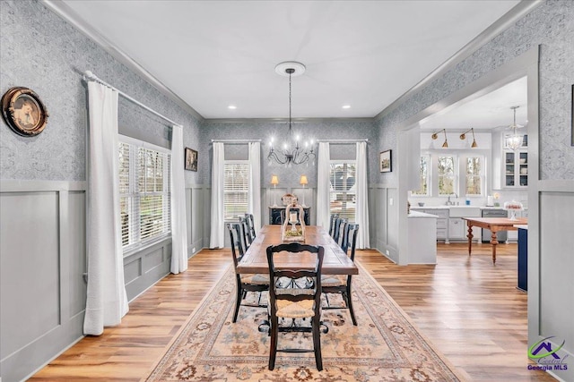 dining room featuring wallpapered walls, light wood finished floors, a wainscoted wall, and an inviting chandelier