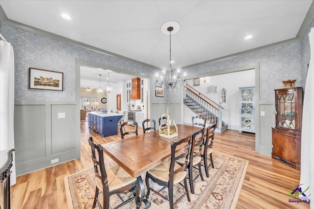 dining space with a notable chandelier, wallpapered walls, light wood-style flooring, wainscoting, and stairs