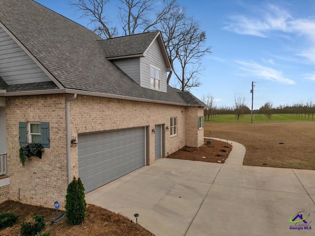 view of side of home with driveway, brick siding, and roof with shingles