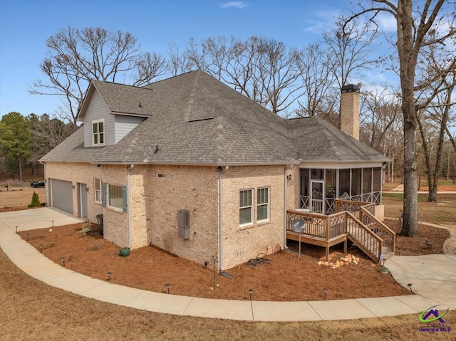 view of side of property with brick siding, a chimney, a shingled roof, a sunroom, and driveway