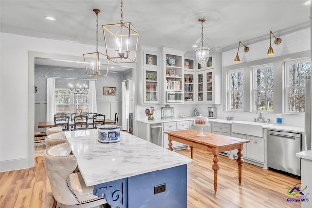 kitchen featuring light wood-type flooring, dishwasher, hanging light fixtures, and a sink