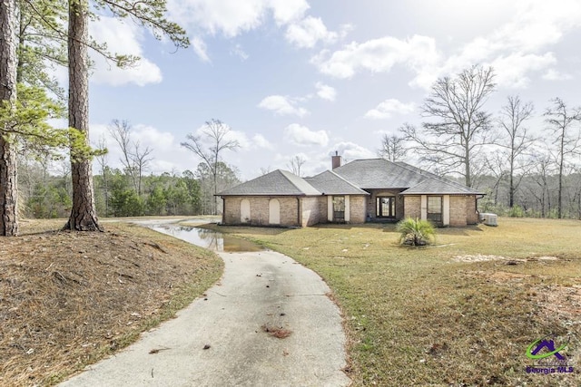 view of front of home featuring a front yard, brick siding, a chimney, and roof with shingles