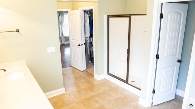 full bath featuring baseboards, tile patterned flooring, a walk in closet, vanity, and a shower stall