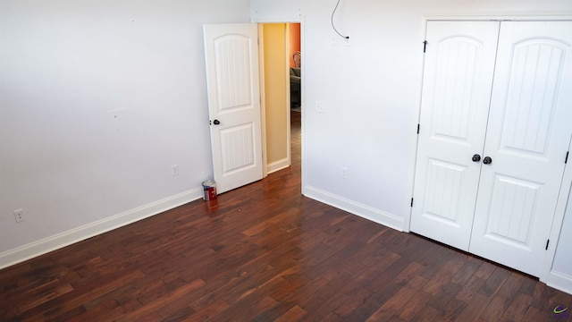 unfurnished bedroom with a closet, baseboards, and dark wood-type flooring