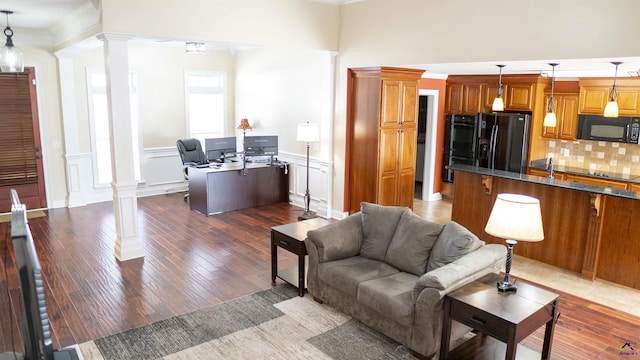 living area featuring a wainscoted wall, wood finished floors, decorative columns, and crown molding