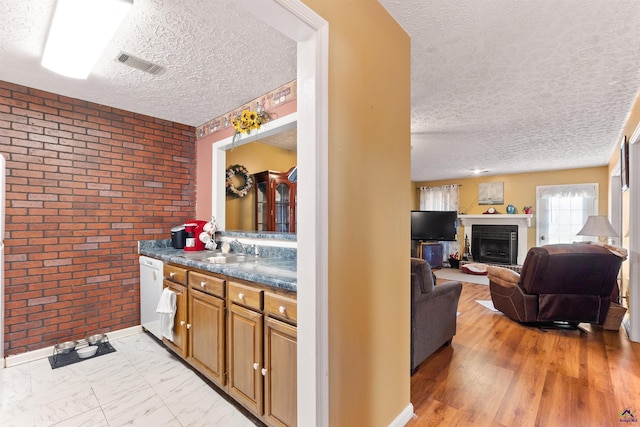 kitchen with marble finish floor, dark countertops, visible vents, a sink, and brick wall