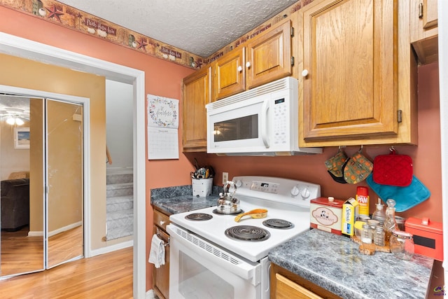 kitchen featuring brown cabinets, a textured ceiling, light wood-type flooring, white appliances, and baseboards