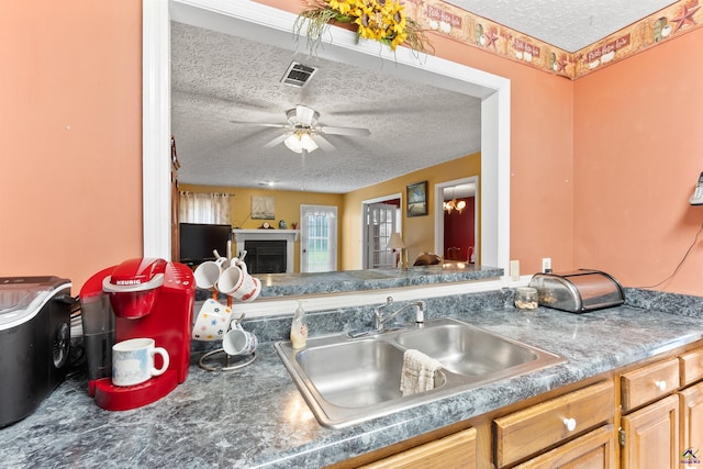 kitchen with a textured ceiling, ceiling fan, a fireplace, a sink, and visible vents