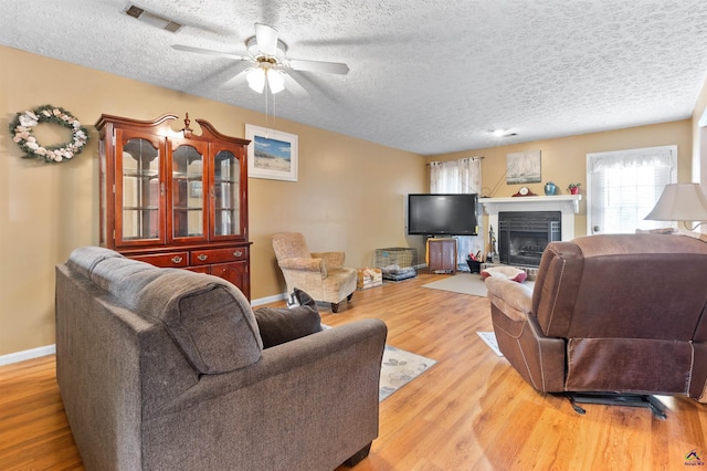 living area featuring baseboards, visible vents, a fireplace with raised hearth, a textured ceiling, and light wood-style floors