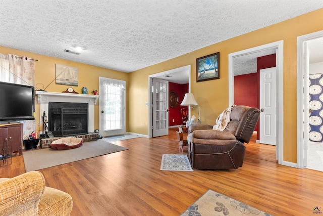 living room with baseboards, visible vents, a fireplace with raised hearth, wood finished floors, and a textured ceiling