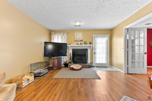 living room with visible vents, a fireplace with raised hearth, a textured ceiling, wood finished floors, and baseboards