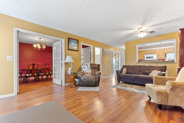 living area featuring light wood-type flooring, french doors, a textured ceiling, and baseboards