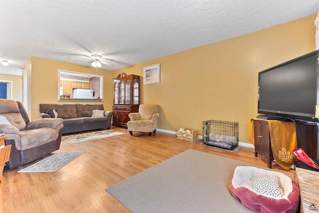 living area with a textured ceiling, wood finished floors, a ceiling fan, and baseboards