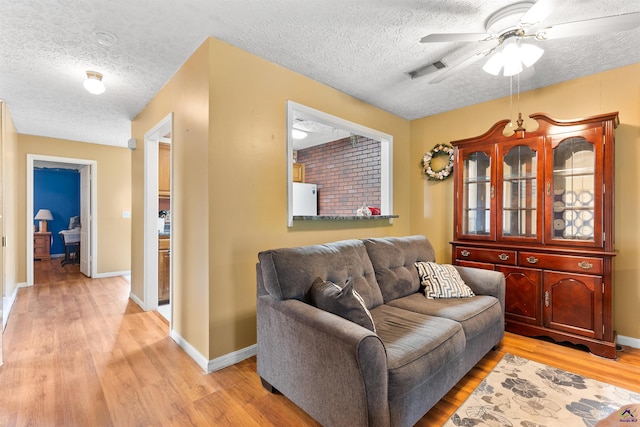 living room featuring a ceiling fan, visible vents, light wood-style flooring, and baseboards