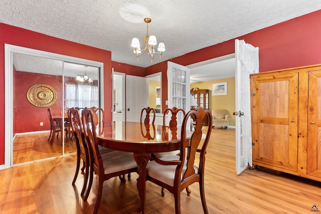 dining room with a chandelier, a textured ceiling, baseboards, and light wood-style floors