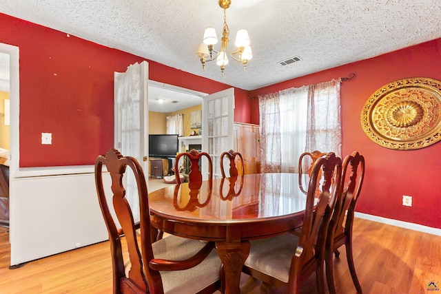 dining space featuring a notable chandelier, a textured ceiling, visible vents, and wood finished floors